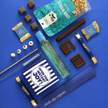 Assorted snacks and a bottle on a blue background with 'Open for Joy' packaging. Inspired by the coast.