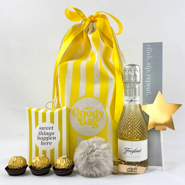 Gift set with a yellow striped bag, small bottle, and decorative items on a white background