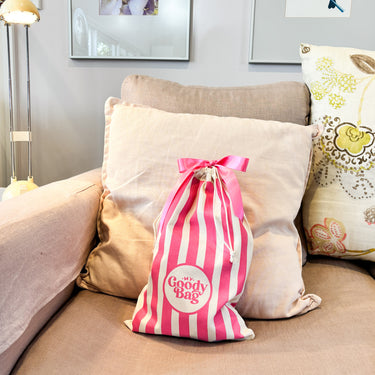 Pink and white striped bag labeled 'My Goody Bag' on a beige couch with pillows.
