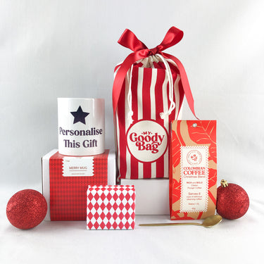 Red My Goody Bag surrounded with coffee, luxury christmas cake (wrapped in red and white giftwrap) and a mug on top of its box which can be personalised through a printing service within My Goody Bag.