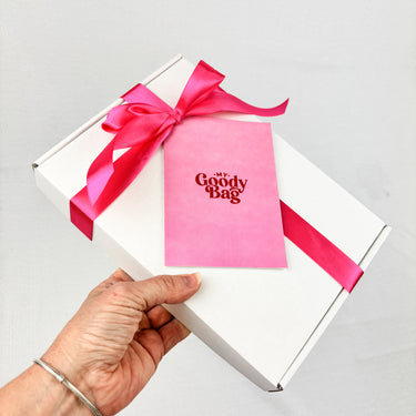 Gift box with pink ribbon and 'My Goody Bag' card held by a hand on a light gray background
