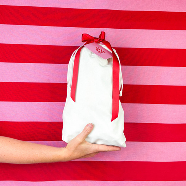 White gift bag with a red ribbon held by a hand against a red and pink striped background