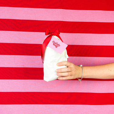White giftbag with red bow held by a hand against a red and pink striped background